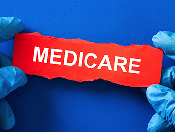 A red paper with the text, "Medicare," and held with two hands wearing blue gloves.