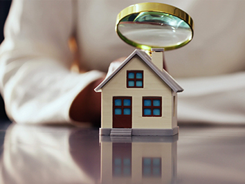 Person examining a toy house with a magnifying glass.